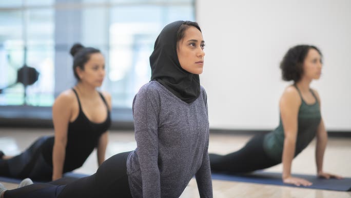 Three women do Yoga in a group lesson. Each person has chosen different types of clothing for their Yoga class. 