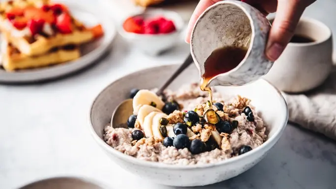 Woman pouring maple syrup onto banana and blueberry porridge
