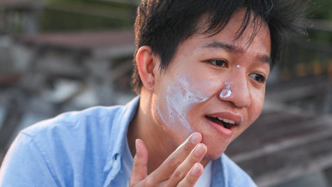 A man is applying sunscreen to his face thinking about how much sunscreen to apply on his face. 