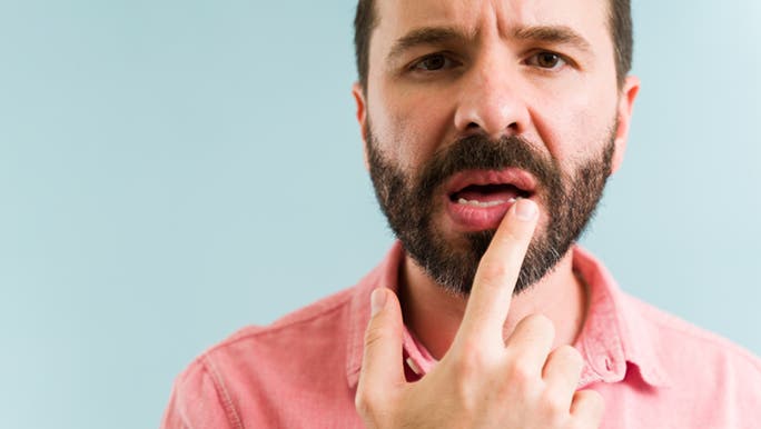 A man with a beard and collared shirt looks concerned as he touches his lips, thinking he has dry lips after alcohol.
