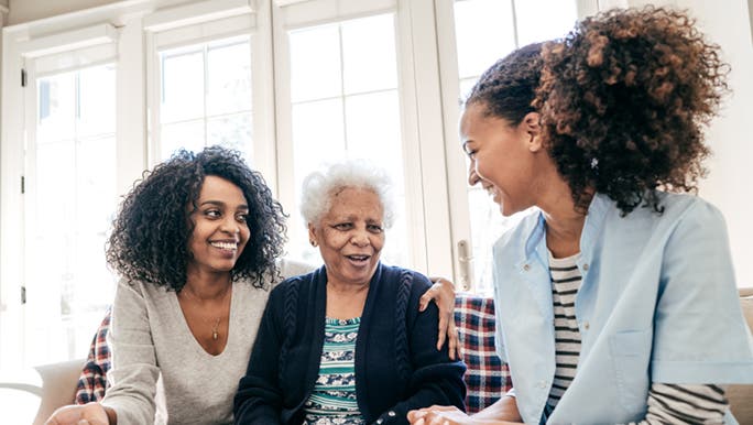 Two daughters are sitting on a couch with their mother as they are caring for one of their elderly parents in Australia.