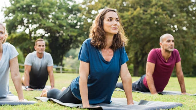 Woman and men in the park doing yoga, the are forming healthy habits. 