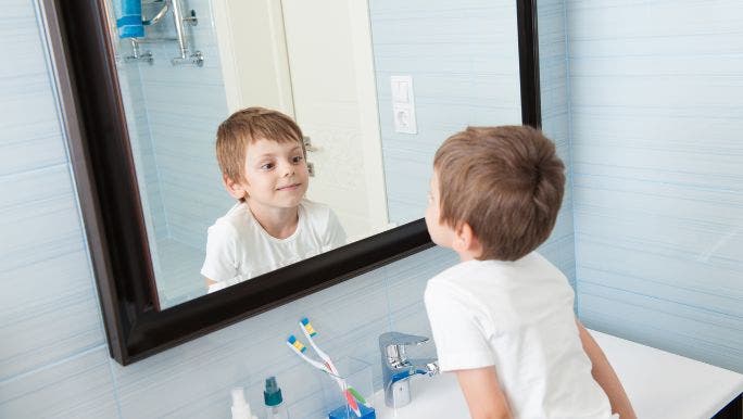 A young boy is looking at himself in a bathroom mirror and smiling