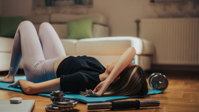 A lady lays on the floor, her muscles hurt after exercise. 