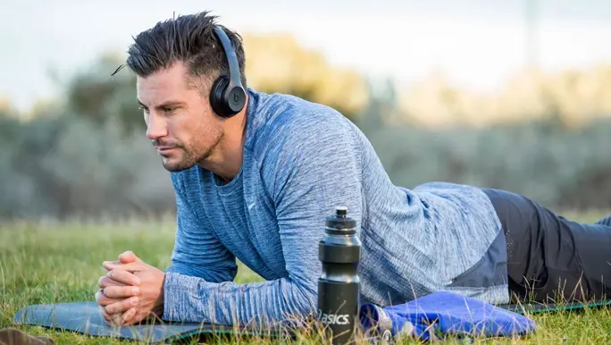 Sam Wood relaxing and listening to music on a yoga mat outside on the grass