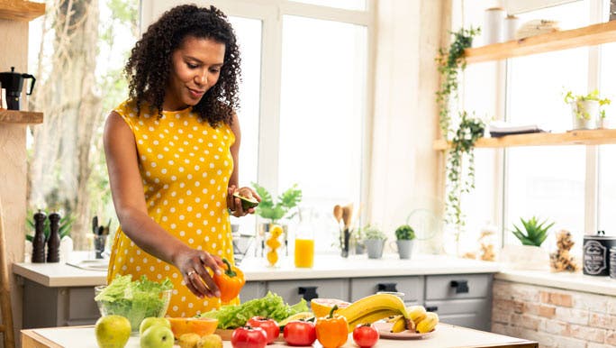 In an open and light kitchen, a woman in a yellow polka dot dress prepares foods to reset her gut.