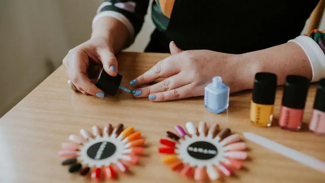 A person paints their nails with light blue Hanami nail polish. Two nail colour wheels are in view in the foreground and a line up of Hanami nail polish bottles are in view.