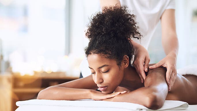 A lady is laying on a massage bed with her eyes closed. It looks like she is getting a remedial massage. 