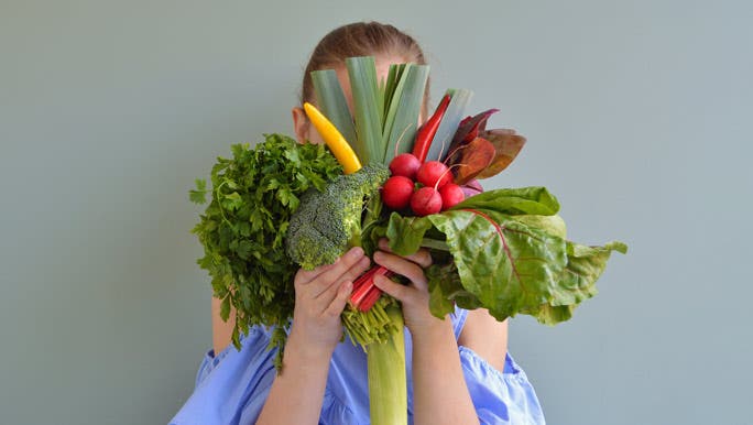 Girl holding a bunch of colourful vegetables in front of her face