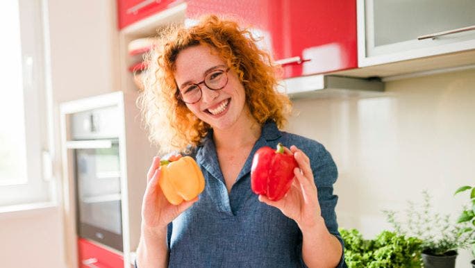 A young woman is smiling as she holds a yellow and red capsicum