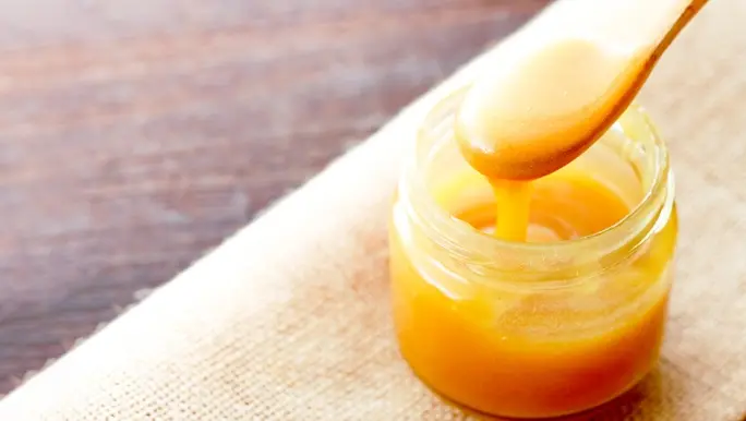 Manuka honey on a wooden spoon being scooped out of a jar