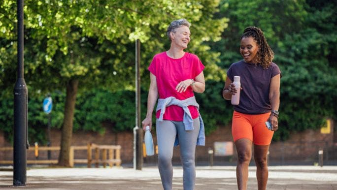 Two women are walking and chatting in a park on a sunny day
