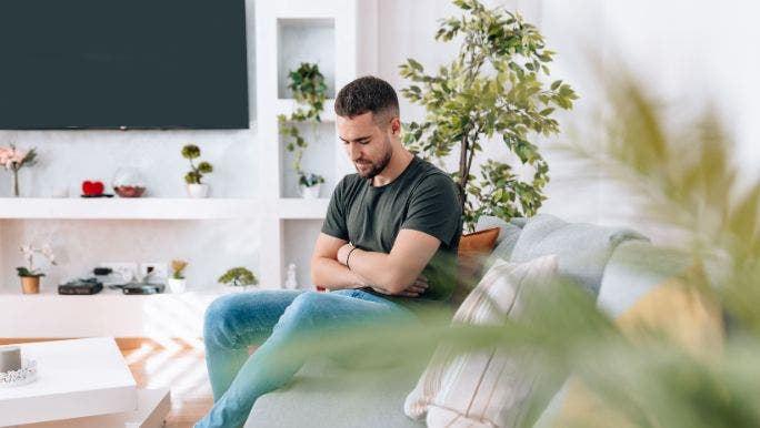Young man sitting on grey couch holding his gut in pain.