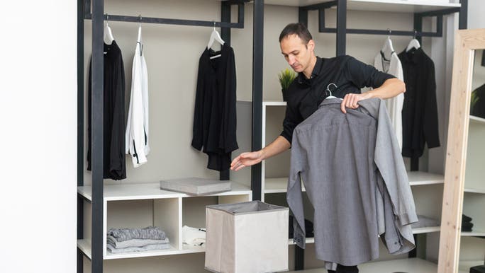 A young Caucasian man is holding business shirts as he organises his wardrobe