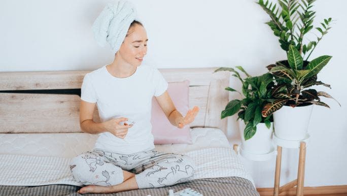 A young woman is sitting on a bed and looking at her fingernails