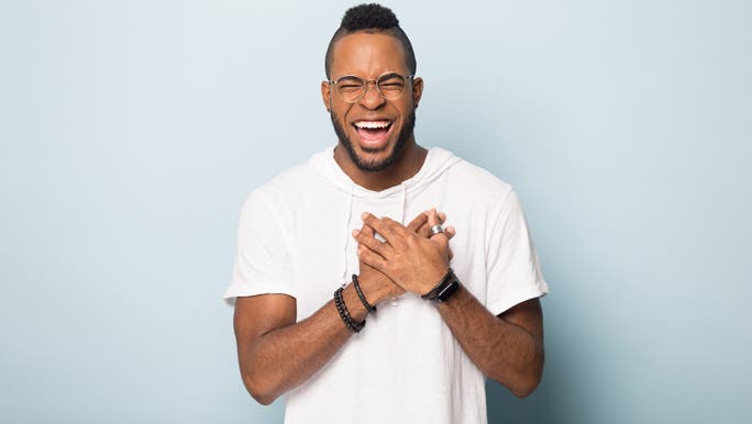 Happy young man, laughing and holding his hands over his heart in gratitude