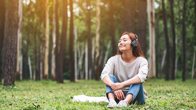 A woman is relaxing in a local park while listening to a podcast about the top 10 causes of stress at work. 