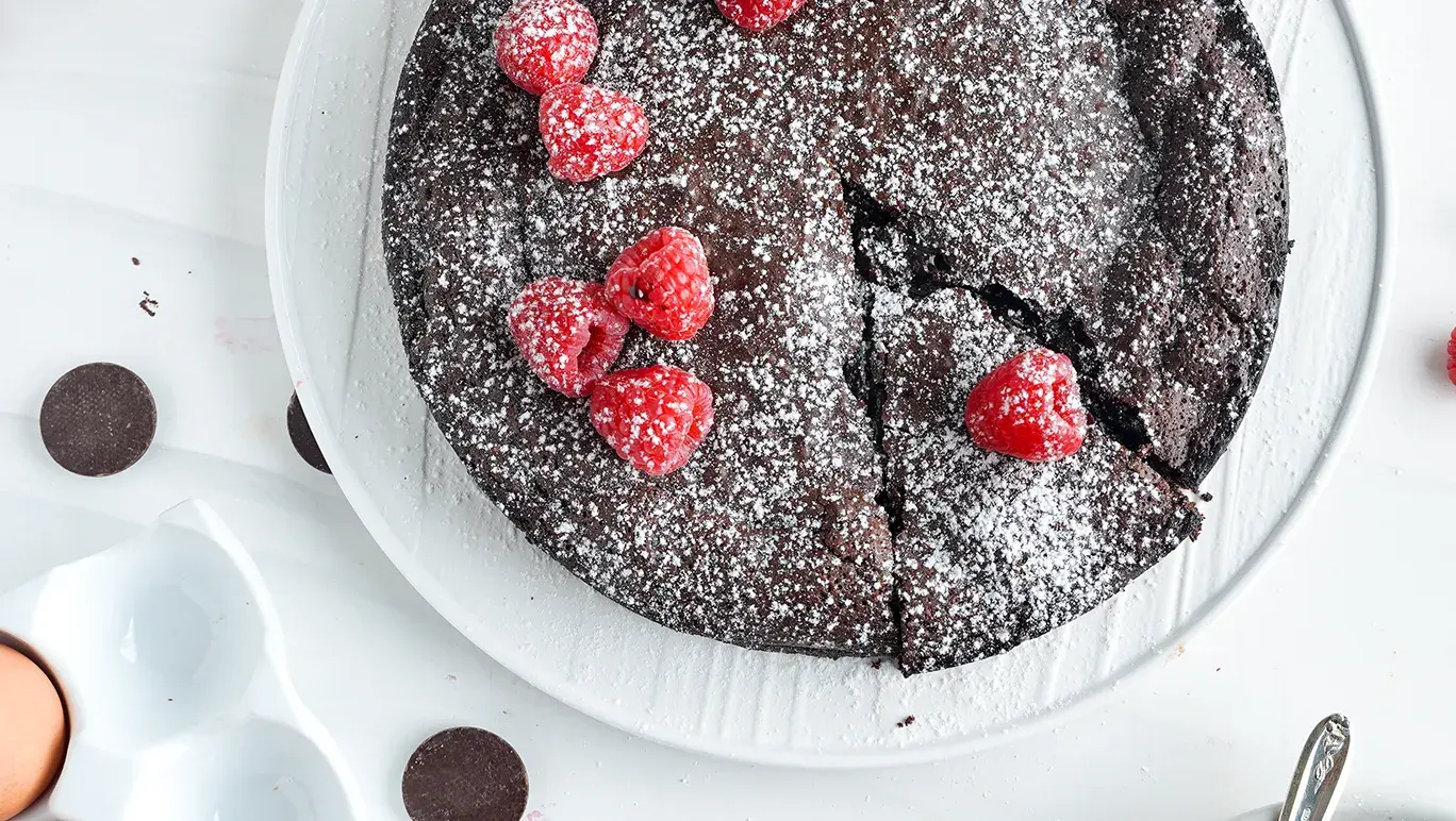 Chocolate mousse cake topped with raspberries on a white bench