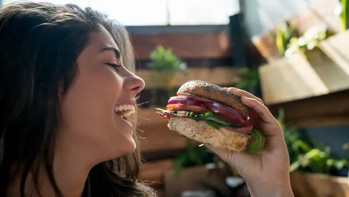 Happy woman with brown hair about to bite into a vegan burger