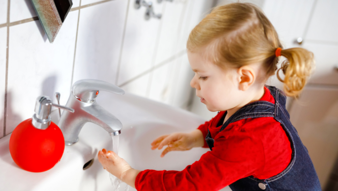 A young toddler is standing at a basin washing her hands