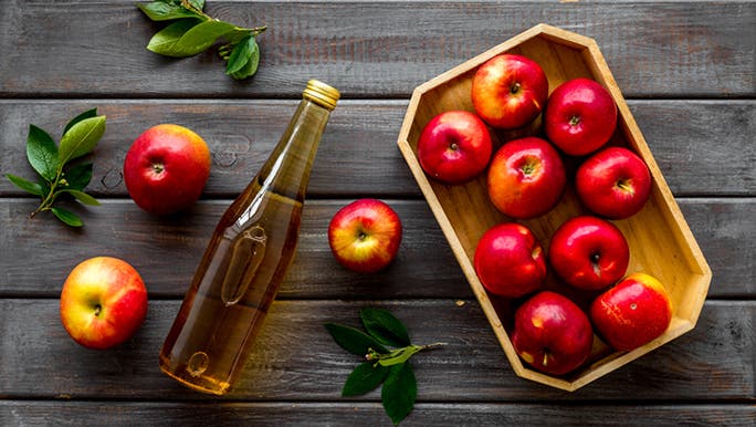 A tray of apples on a wooden table with a bottle of apple cider vinegar