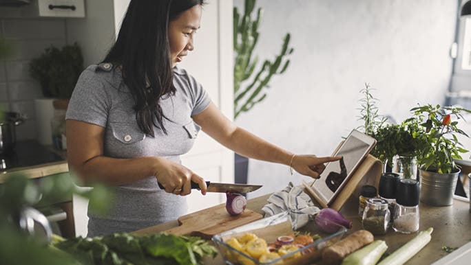 A woman stands in a kitchen preparing a healthy meal from a recipe. Perhaps she is using nutrition as a motivation to lose weight.