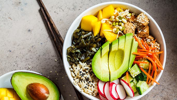 From above, a plant based or vegan bowl of rice and vegetables is on a table next to some chopsticks. 