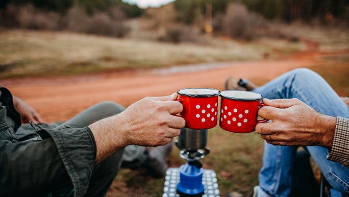 Two red camping cups are being touched together, there is a red earth track in the background. 