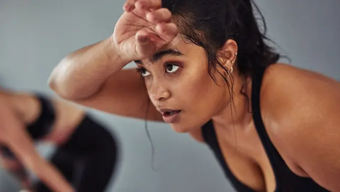 Woman in black active wear wiping sweat from her forehead