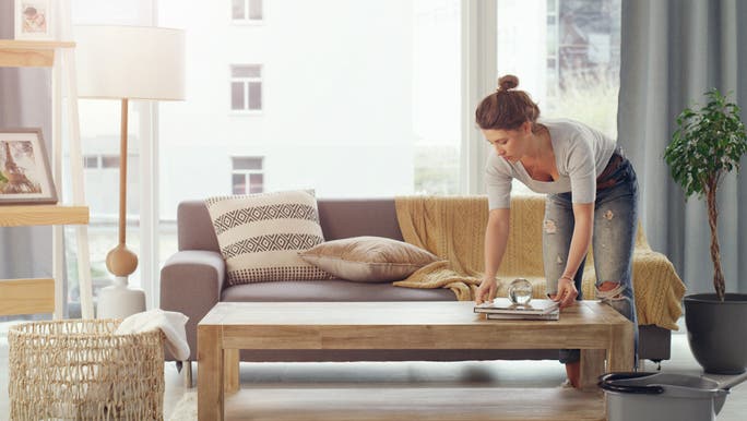A young woman is tidying up a coffee table as part of decluttering her home