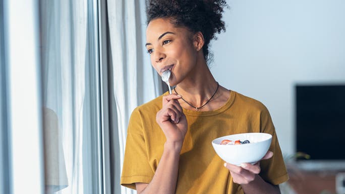 A woman with a dark complexion is smiling as she eats a bowl of fruit