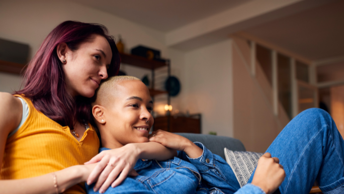 Two young women are smiling and cuddling on a sofa