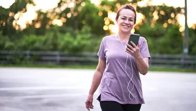 Woman walking at sunset, she is smiling and holding a smartphone