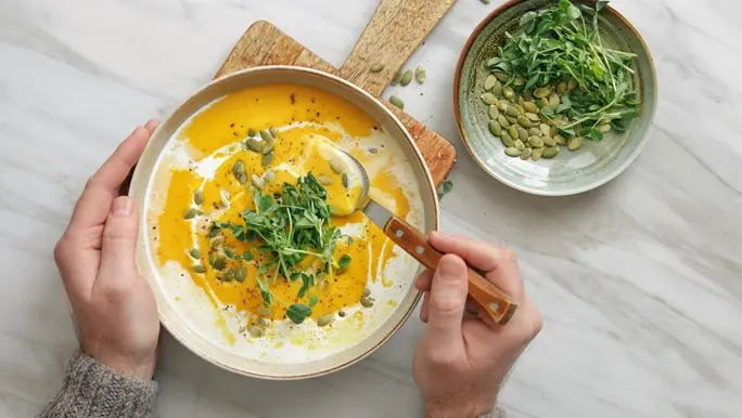 A bowl of creamy pumpkin soup with pepitas and greens