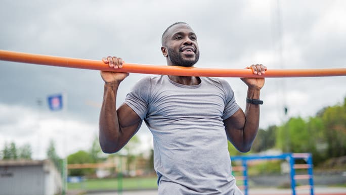 A man is doing a pull up outside on an orange bar and is thinking about how you get better at pull ups. 