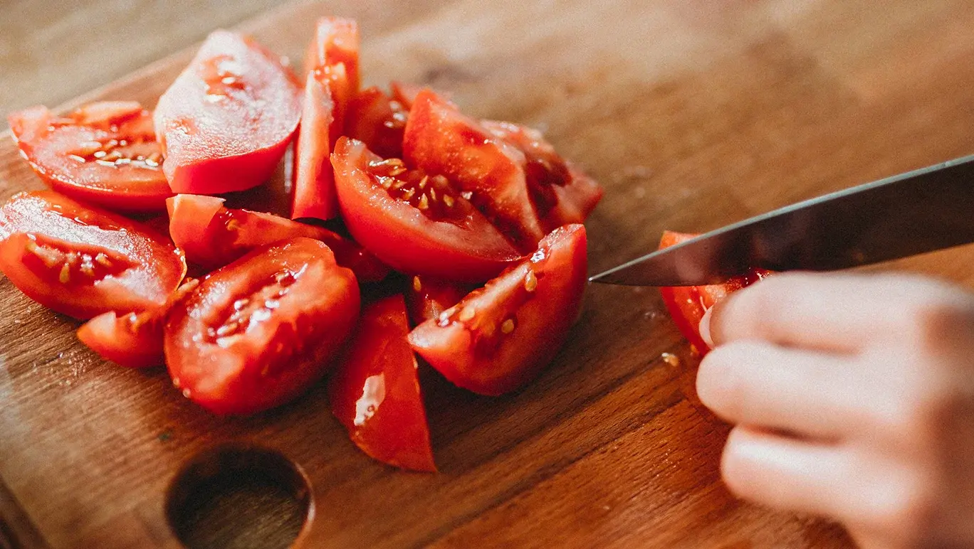 Person chopping up a tomato on a chopping board.
