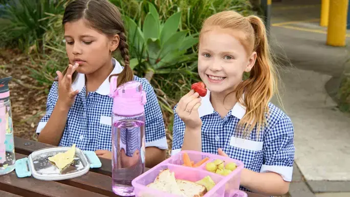 Girl with red hair in a blue and white uniform eating a low fodmap lunch at school