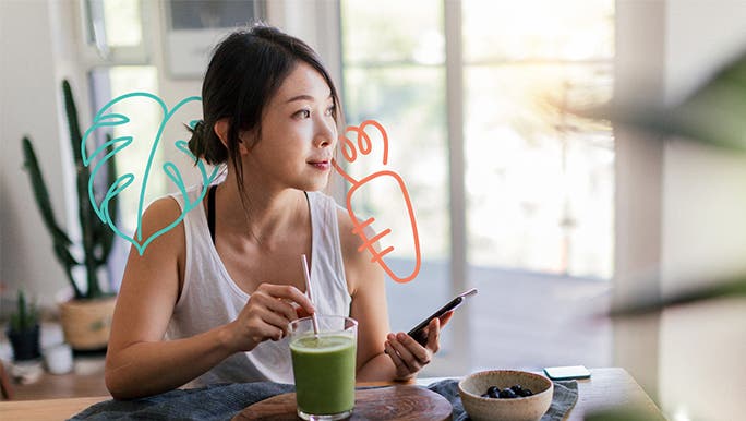 Young woman in the kitchen drinking a green smoothie and scrolling on her phone