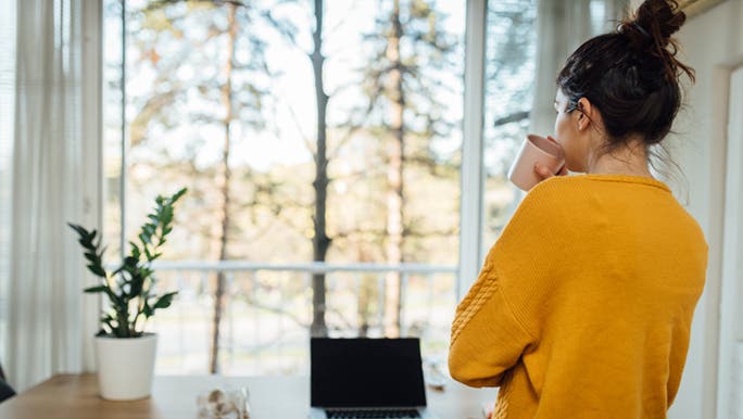  A woman in a mustard jumper is facing away from the camera, she is drinking coffee and perhaps doing an exercise to improve focus.