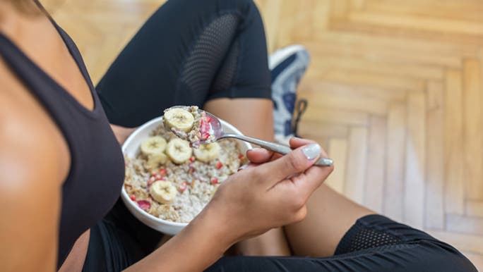 A young woman in activewear eats a bowl of oatmeal and banana before a workout.