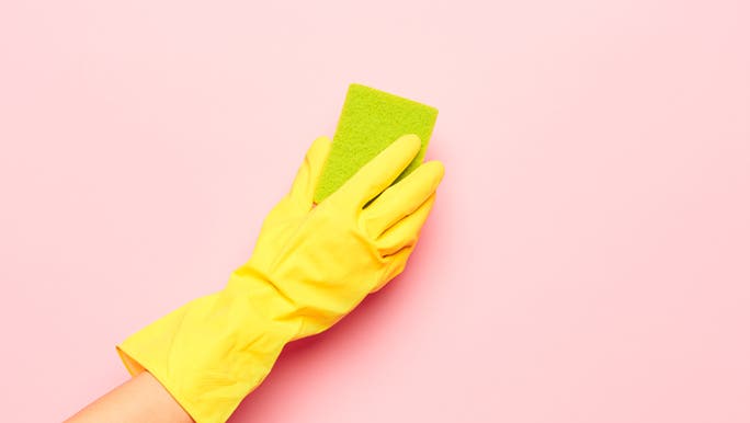 A gloved hand is cleaning a brightly coloured wall with a bright green sponge which may be a way to clean black mould.