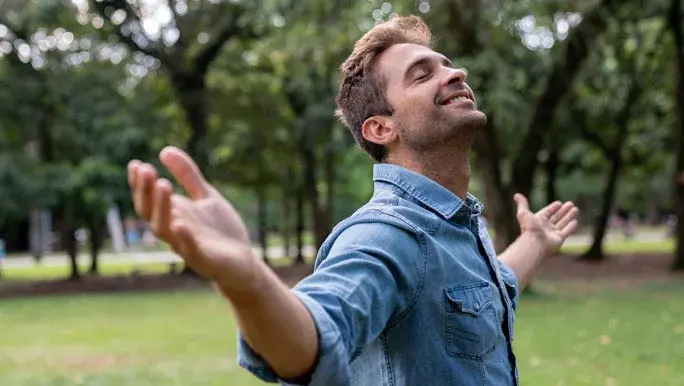 peaceful man relaxing at the park with arms open and smiling - 