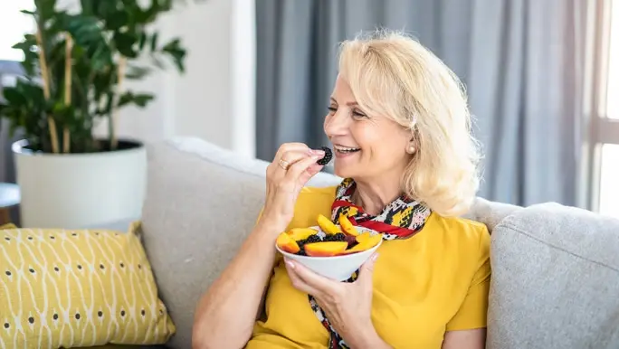Woman relaxing on the couch at home enjoying a snack of fresh berries and peaches