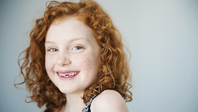A girl smiles at the camera revealing her missing tooth. 