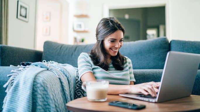 A woman smiles as she works on a laptop at a coffee table, she looks productive. 