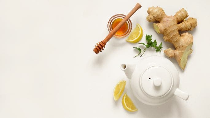 A flat-lay image of a white teapot with ginger, lemon and honey