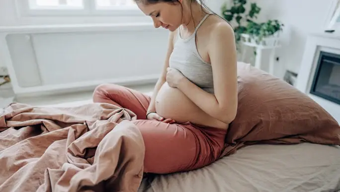Pregnant woman sitting up in bed cradling her belly