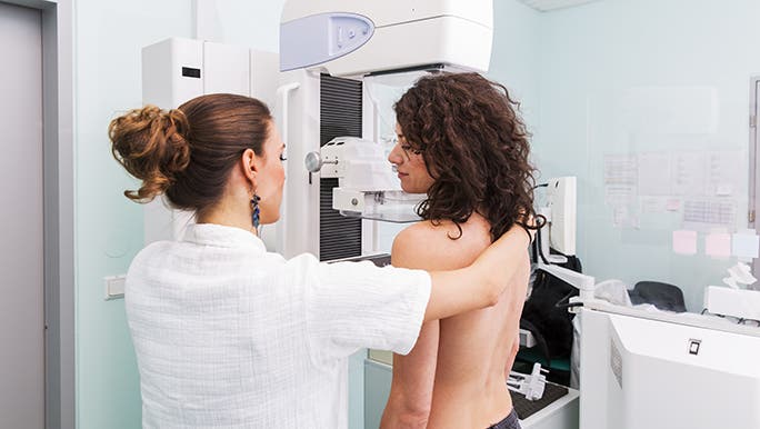 A woman is getting a mammogram. The practitioner is helping her get into the right position in the machine. 