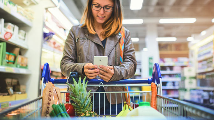 Woman checking her grocery list on her phone and doing her weekly shop at the supermarket