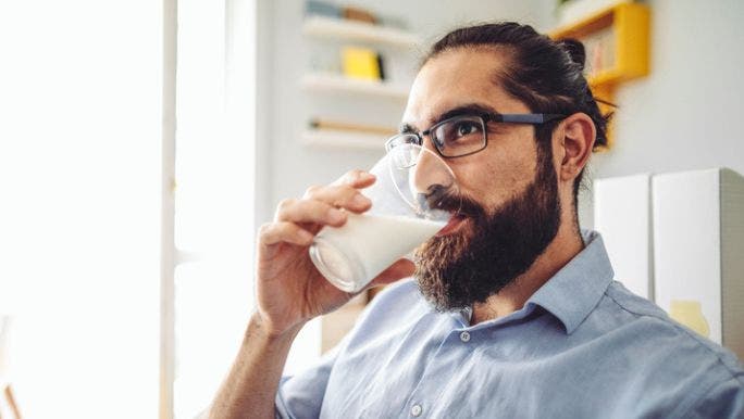 A man wearing glasses is drinking a glass of milk